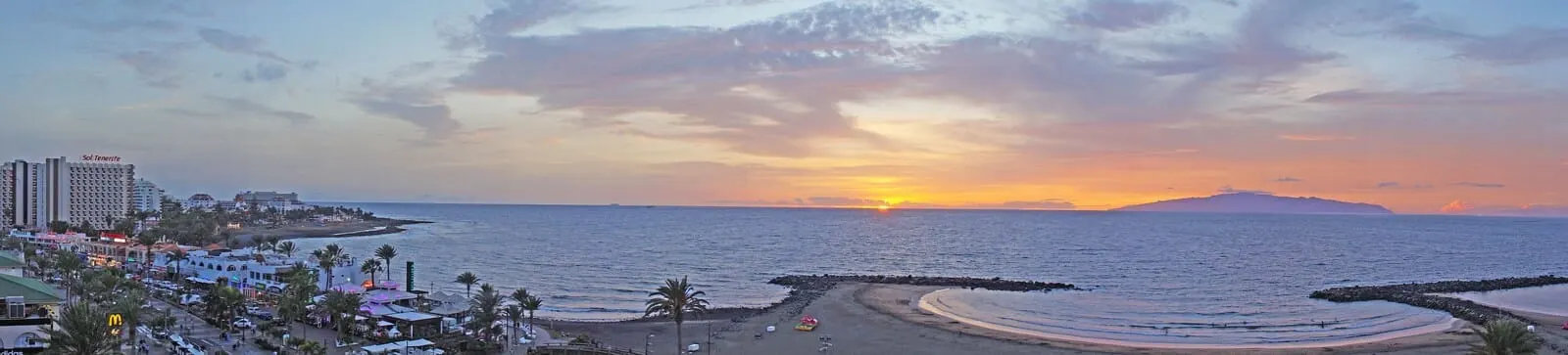 Alexandre Troya: A coastal cityscape with a sunset over the ocean, featuring a beach, a marina