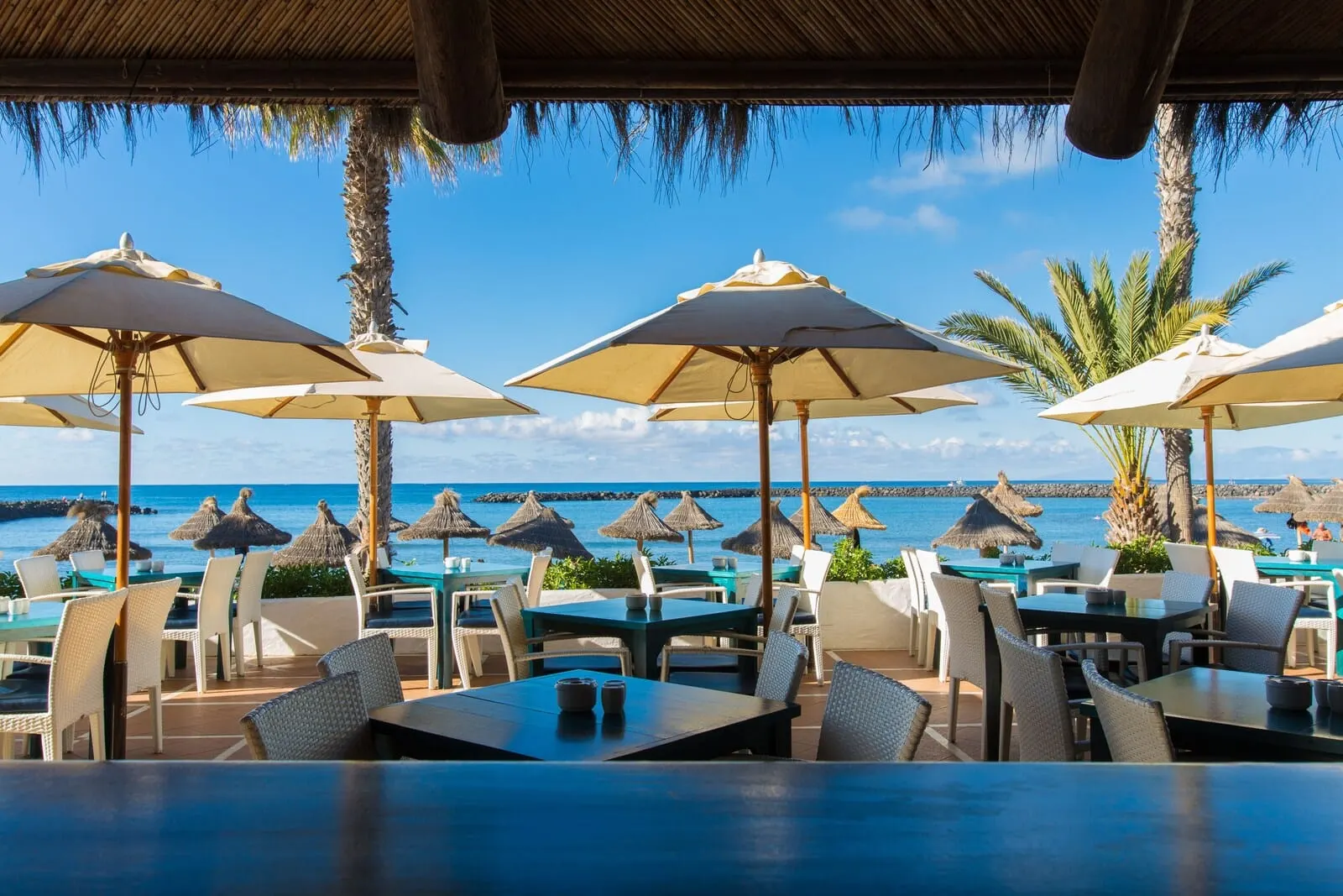 Cleopatra Palace: An outdoor dining area with tables and chairs, umbrellas, and a view of the ocean
