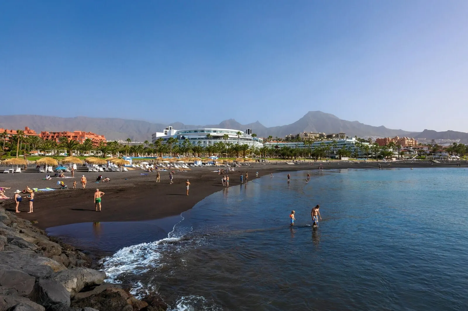 Hotel Riu Palace Tenerife: A beach with a hotel in the background, a rocky shoreline