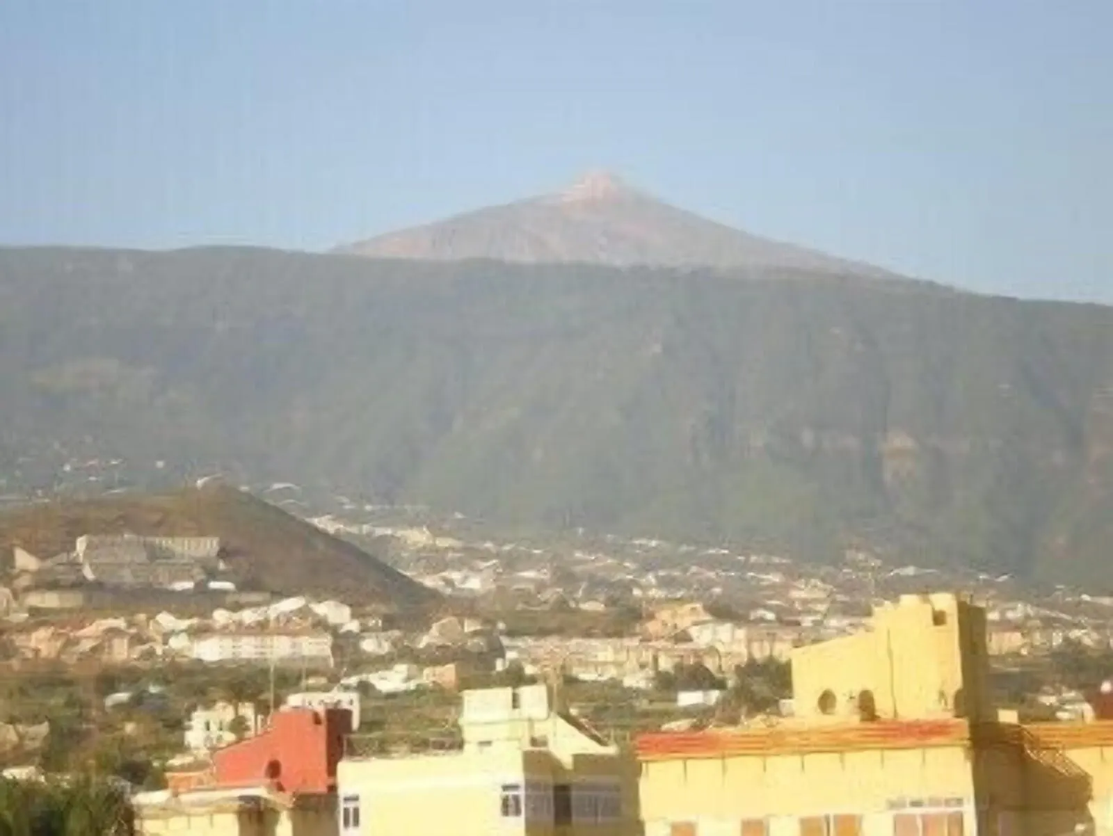 Hotel Tejuma: A mountain with a red peak, surrounded by a town with buildings and a clear sky