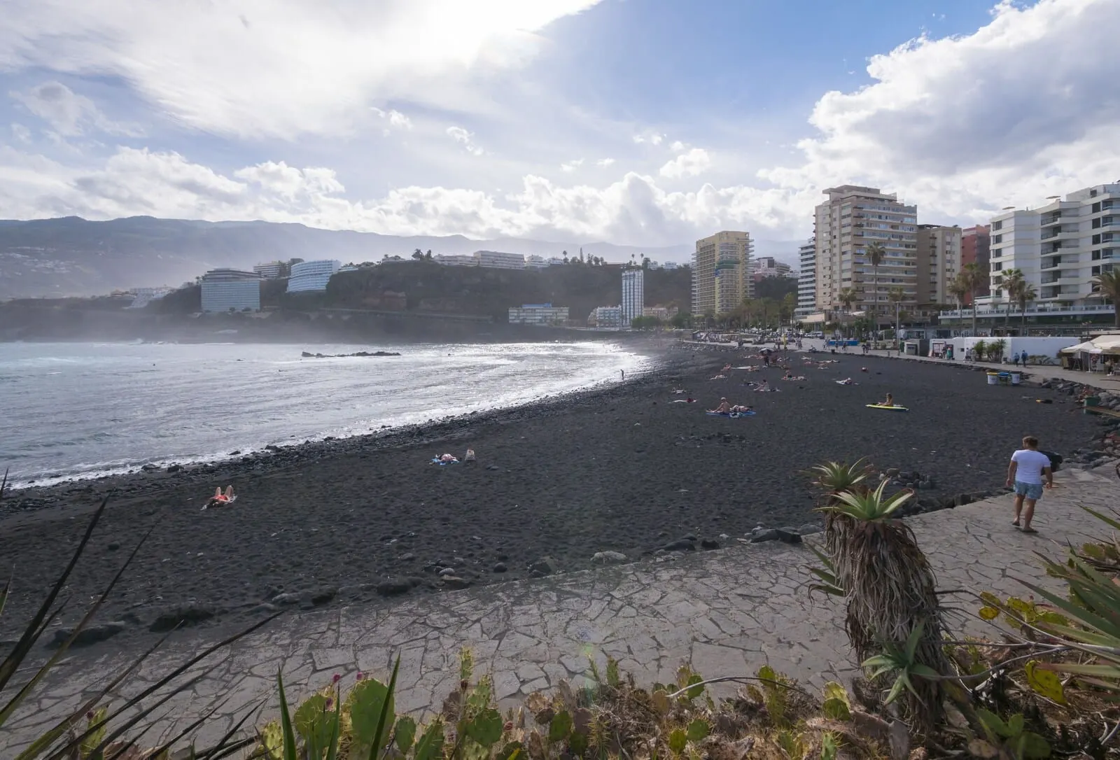 Checkin Concordia Playa: A beach with a rocky shoreline, a few people, and buildings in the background