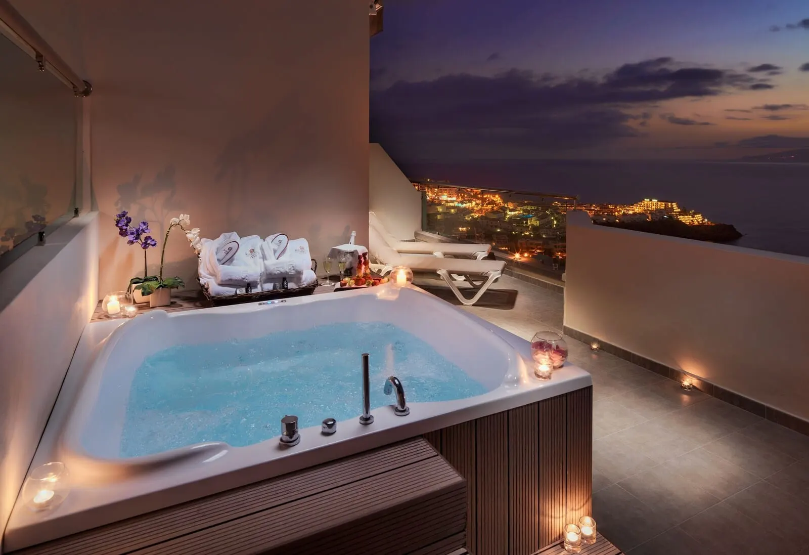 Royal Sun Resort: A spa area with a hot tub, towels, and candles, overlooking a cityscape at dusk