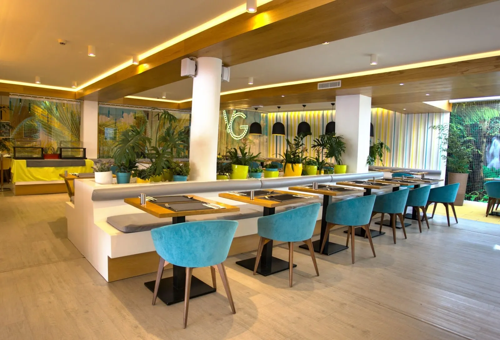 Vanilla Garden Boutique Hotel: A modern restaurant with a long counter, blue chairs, and potted plants