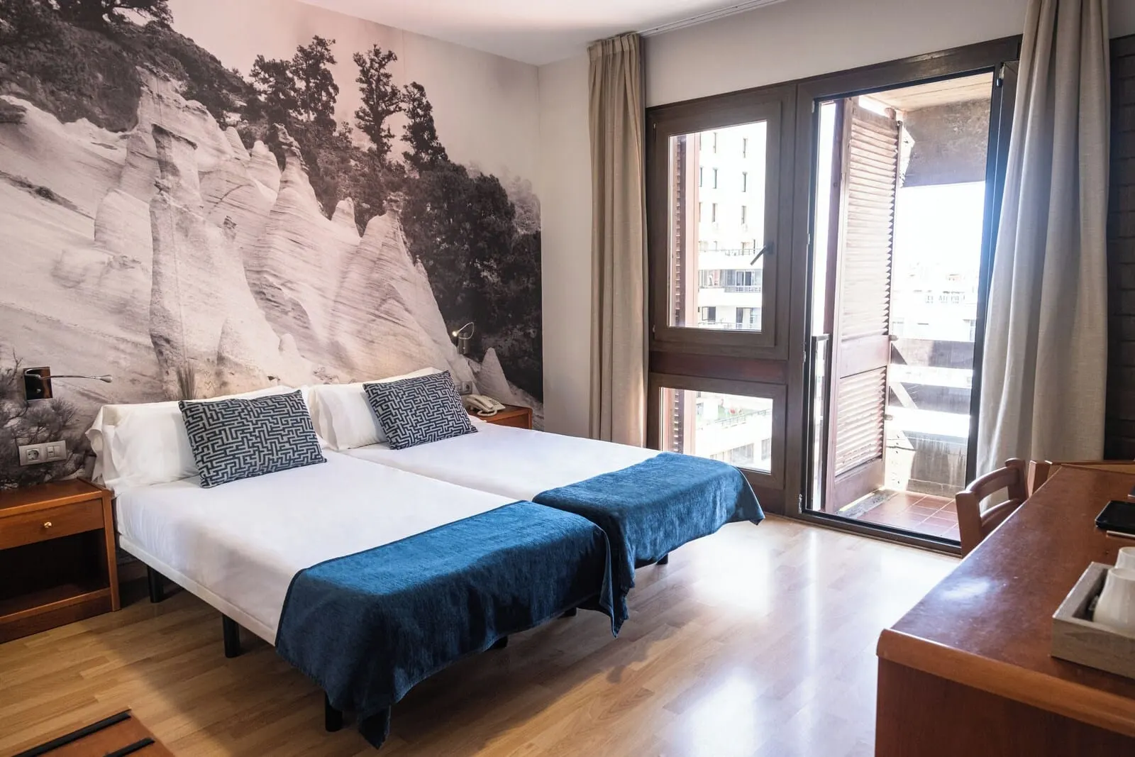 Hotel Adonis Plaza: A hotel room with two beds, a large window, a wooden desk, and a mural on the wall