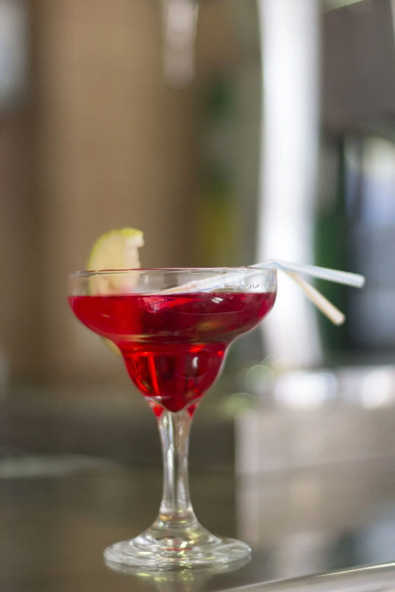 Coral California: A cocktail in a stemmed glass with a lime garnish and a straw