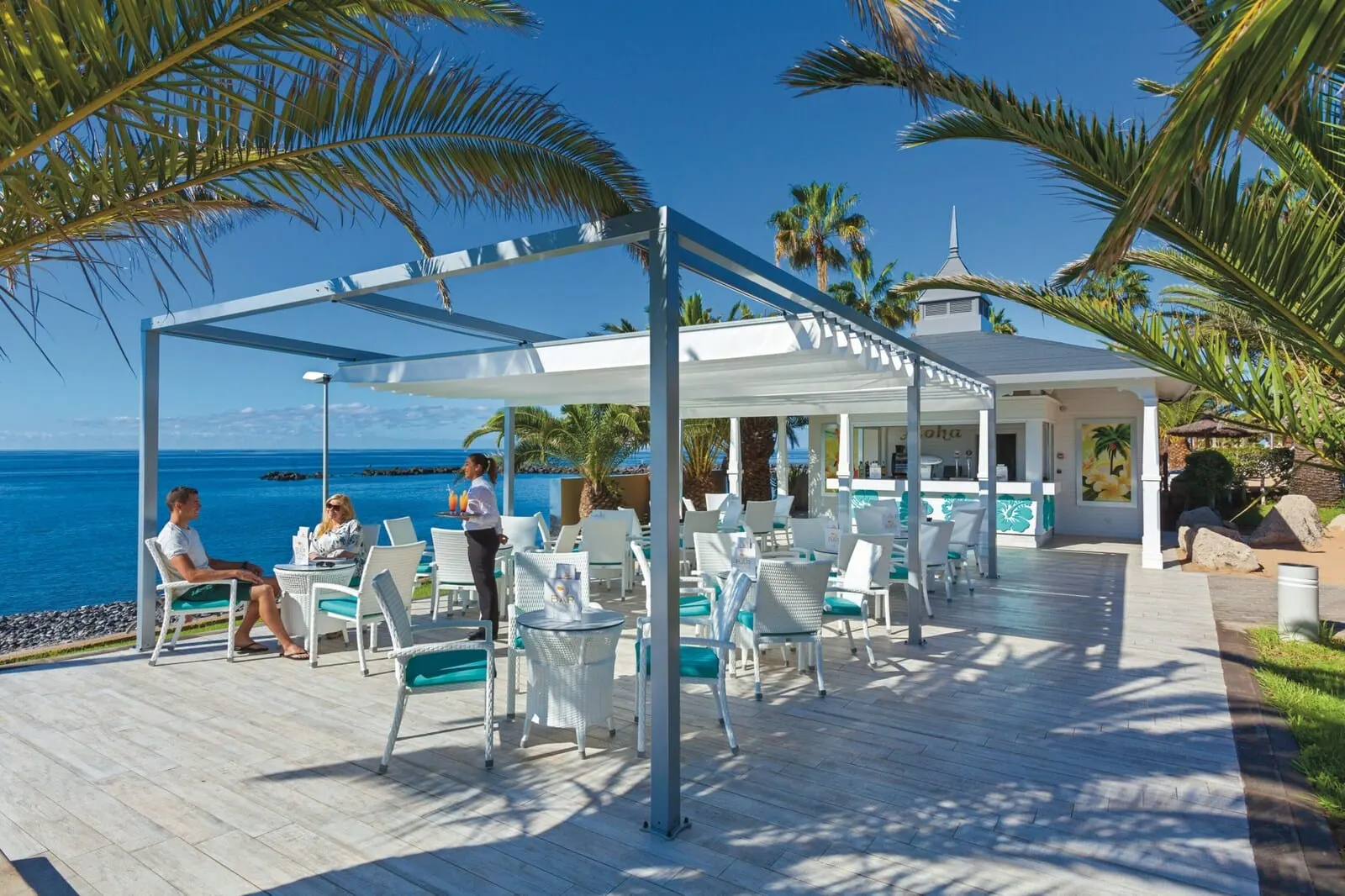 Hotel Riu Arecas: A covered outdoor seating area with white chairs and tables