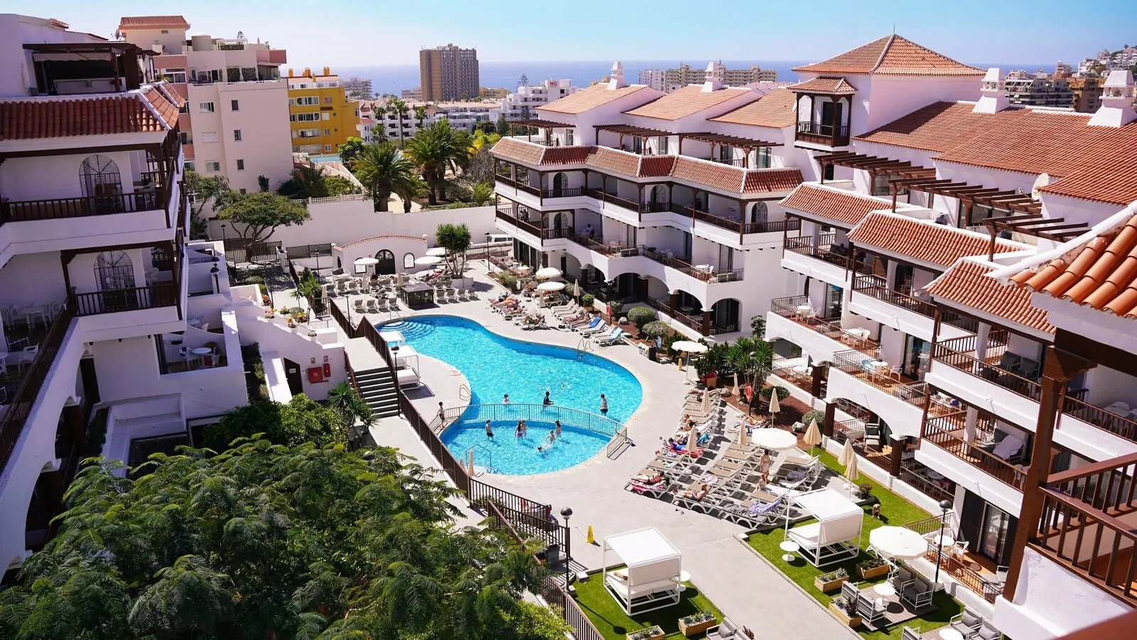 Coral Los Alisios: A resort with a central swimming pool, multiple balconies, and a view of the sea