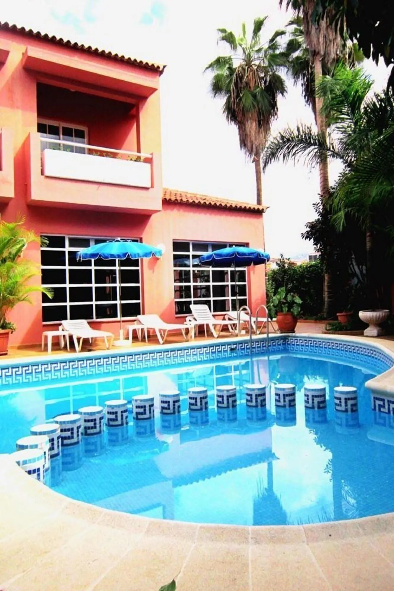 Hotel Don Cándido: A pool area with lounge chairs and umbrellas, a building with a red facade