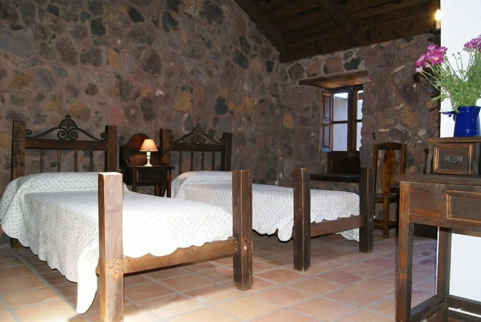 Hotel Rural Caserío Los Partidos: A rustic room with stone walls, two wooden beds with white linens, a wooden table