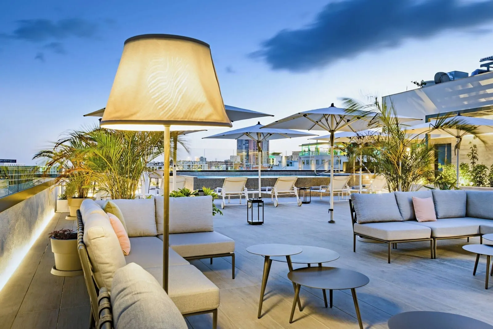 AC Hotel Tenerife: An outdoor seating area with cushioned sofas, round tables, and umbrellas