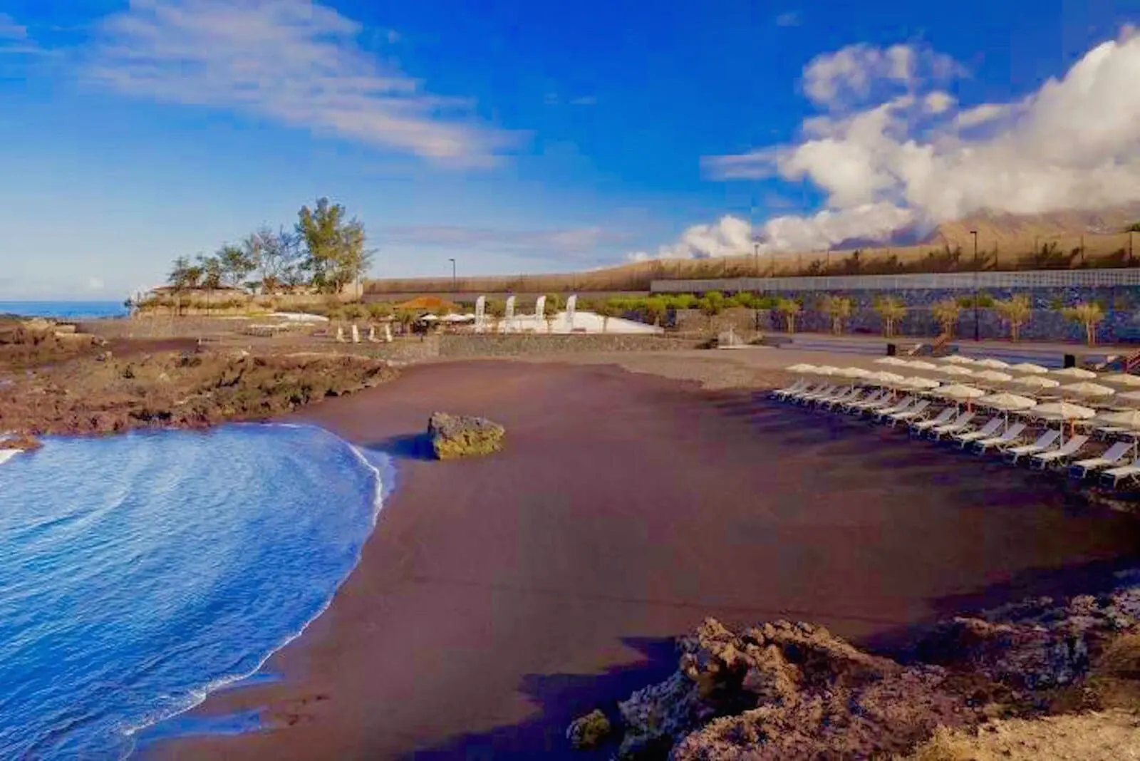 Rok Plaza: A beach with a rocky shoreline, a sandy area with lounge chairs, and a clear sky