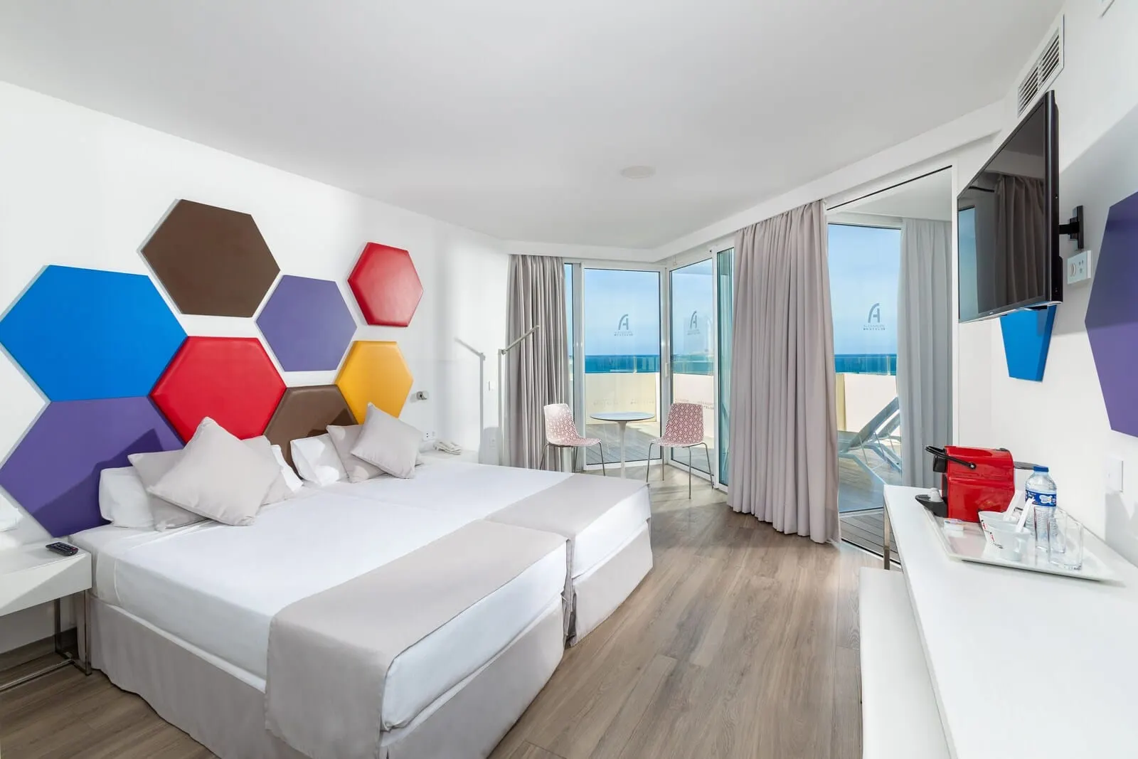Alexandre Troya: A modern hotel room with a large bed, a desk, and a view of the sea