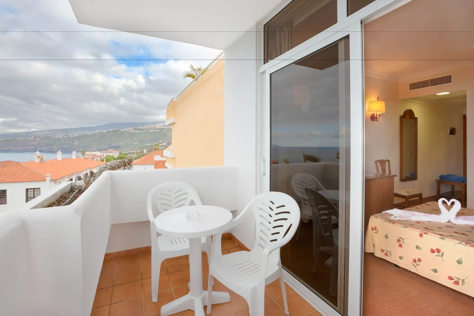 BLUESEA Puerto Resort: A balcony with a table and chairs, a bed with a floral bedspread