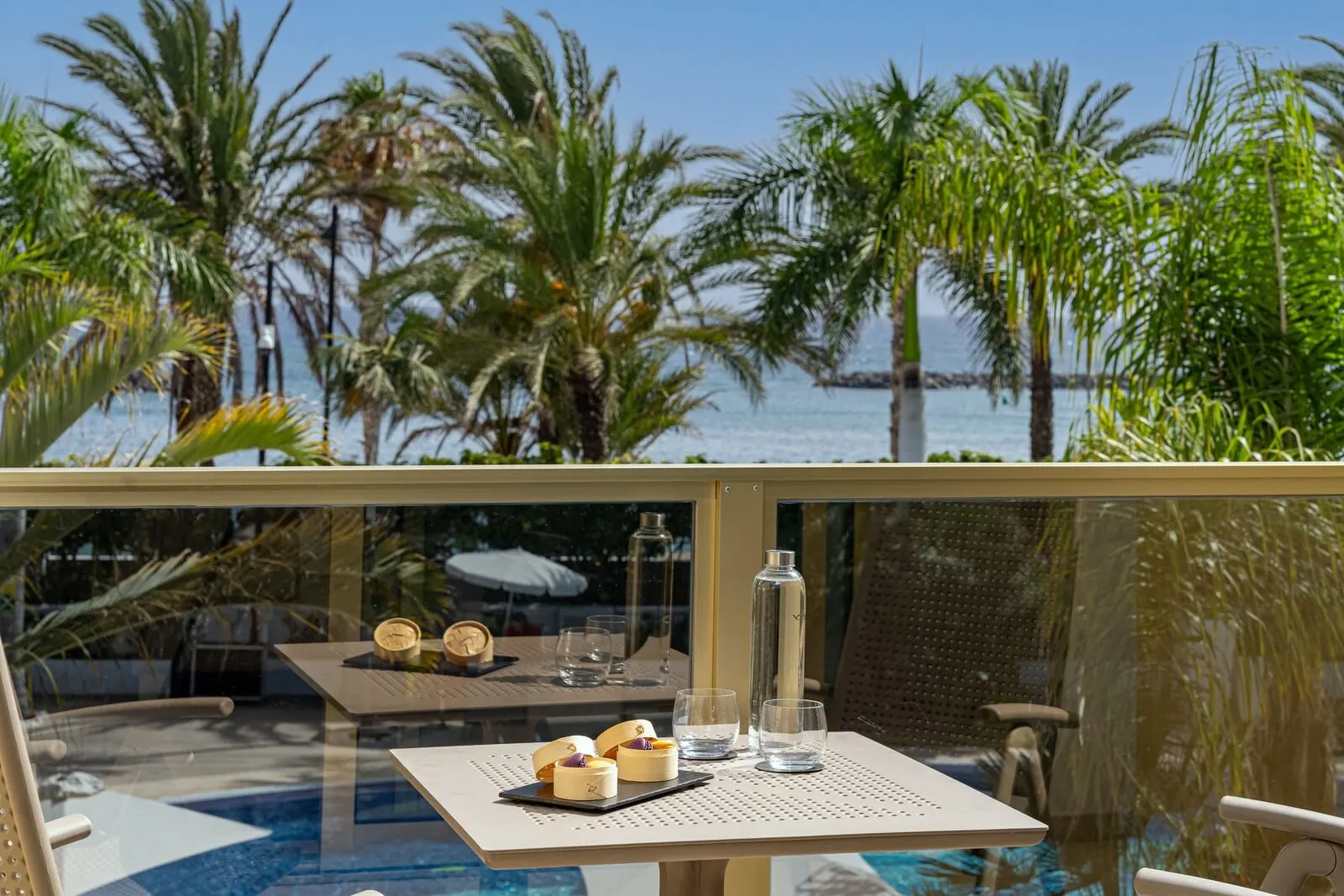 Sir Anthony: A glass-enclosed terrace with a pool, palm trees, and a table with desserts and glasses