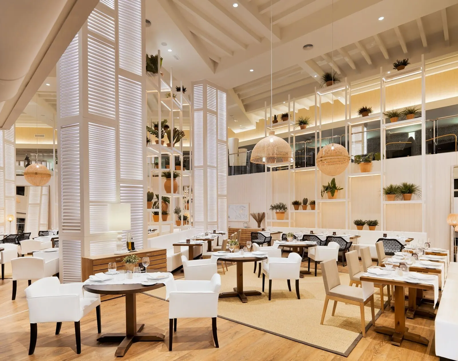 H10 Conquistador: A modern restaurant with white furniture, wooden floors, and potted plants on shelves