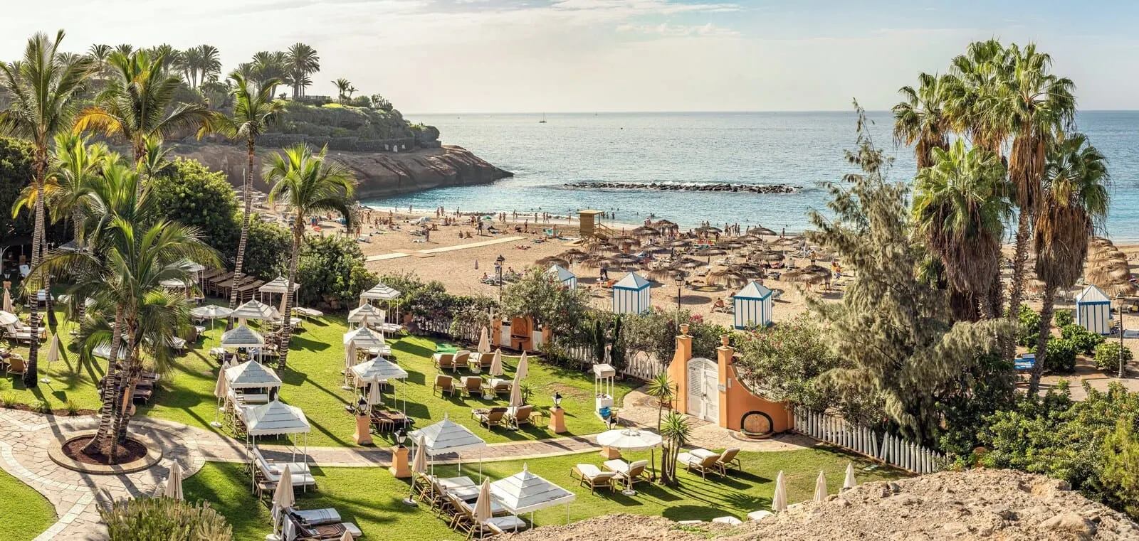 Bahía del Duque: A resort with a beach area, outdoor seating, and palm trees