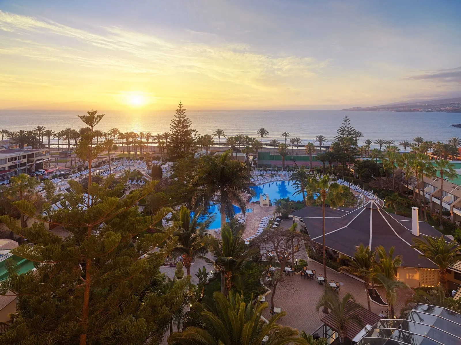 H10 Las Palmeras: A resort with a pool, palm trees, and a view of the ocean at sunset