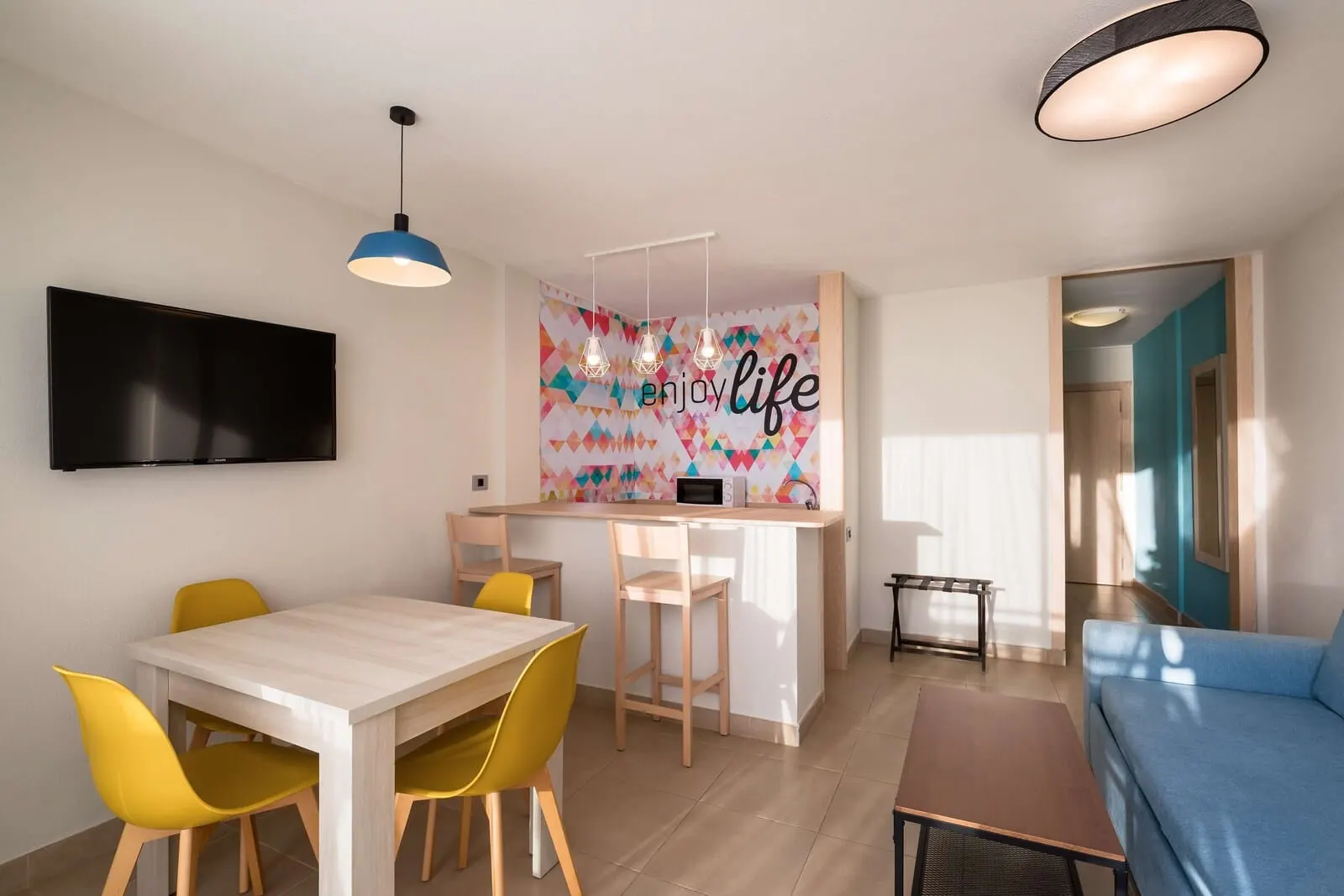 Servatur Isora Suites: A modern living room with a sofa, a dining table with yellow chairs