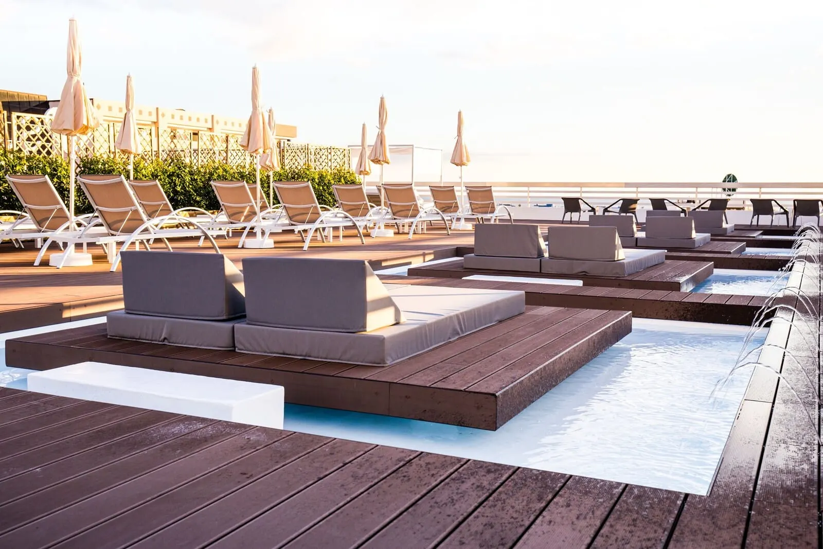 Coral Suites & Spa: A poolside area with lounge chairs and sunbeds, a wooden deck, and a view of the ocean