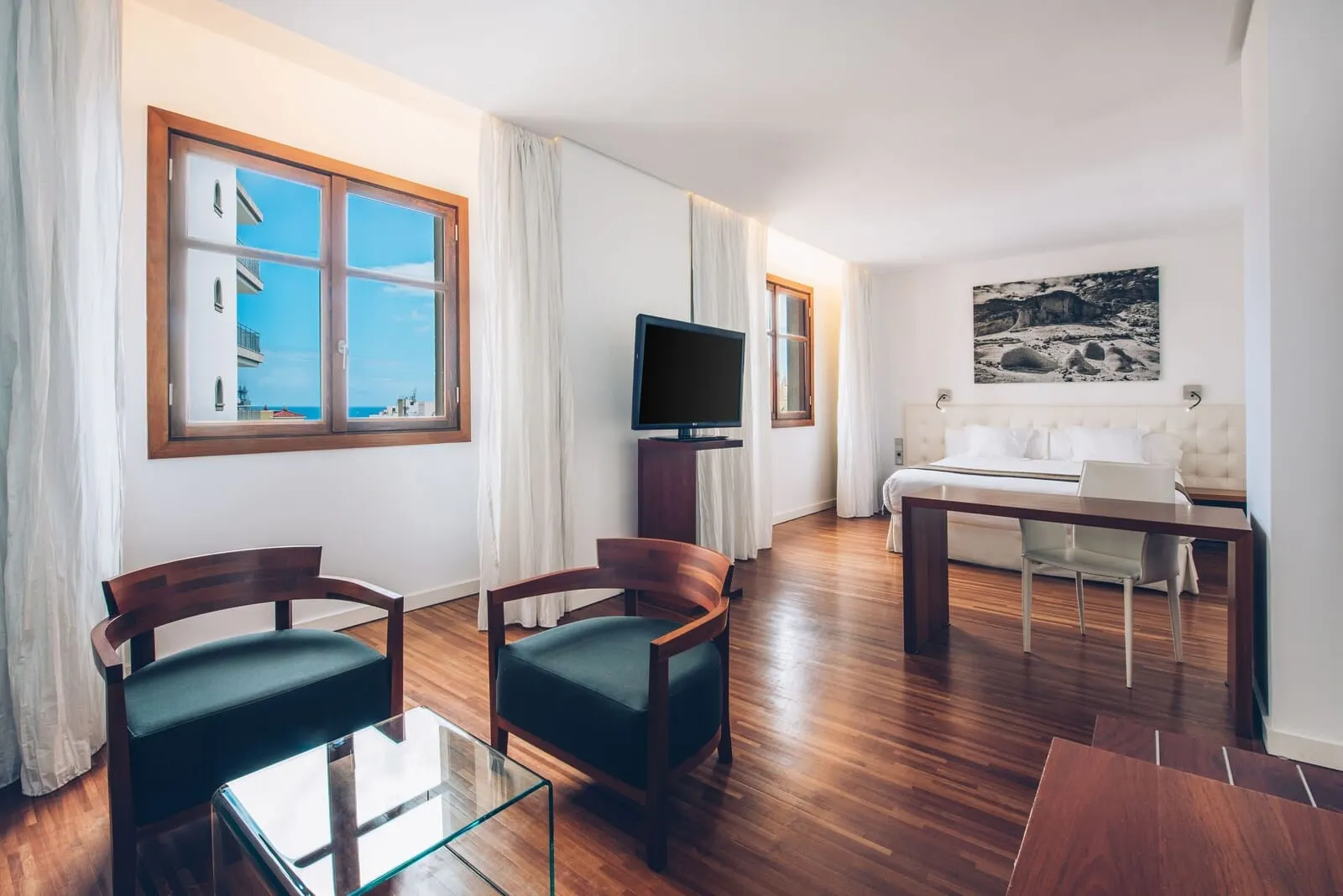 Iberostar Heritage Grand Mencey: A modern living room with a wooden floor, a glass coffee table, two upholstered chairs