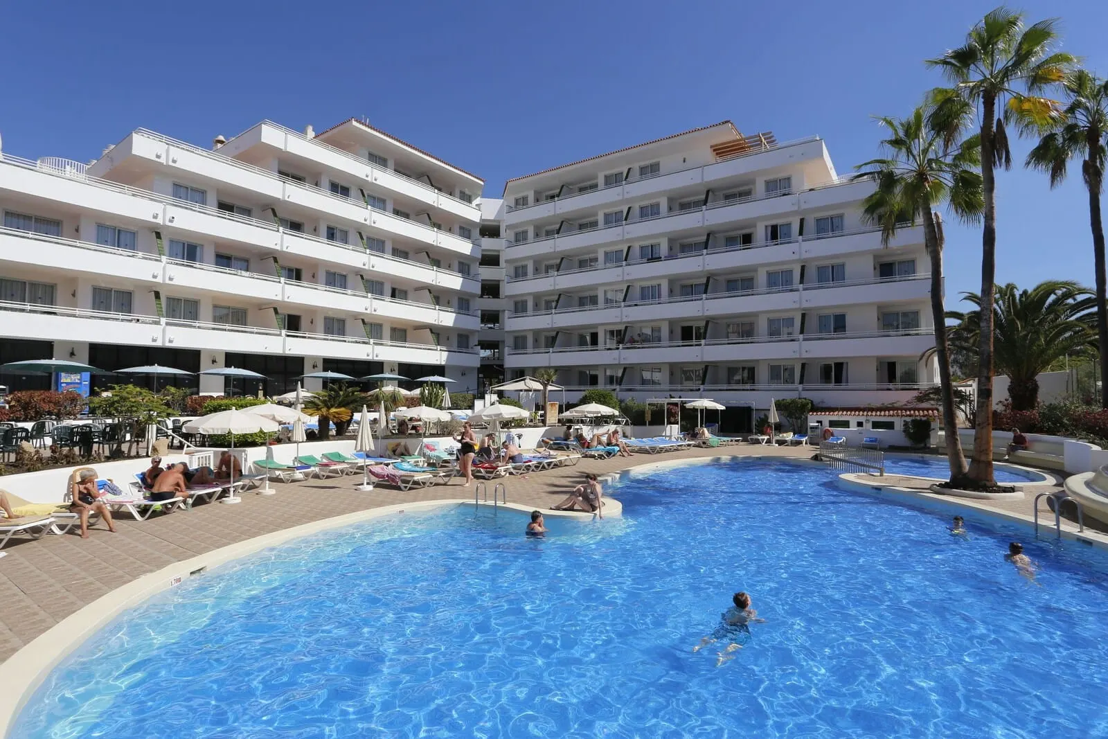 Hotel Andorra: A hotel with a large swimming pool surrounded by sun loungers and palm trees