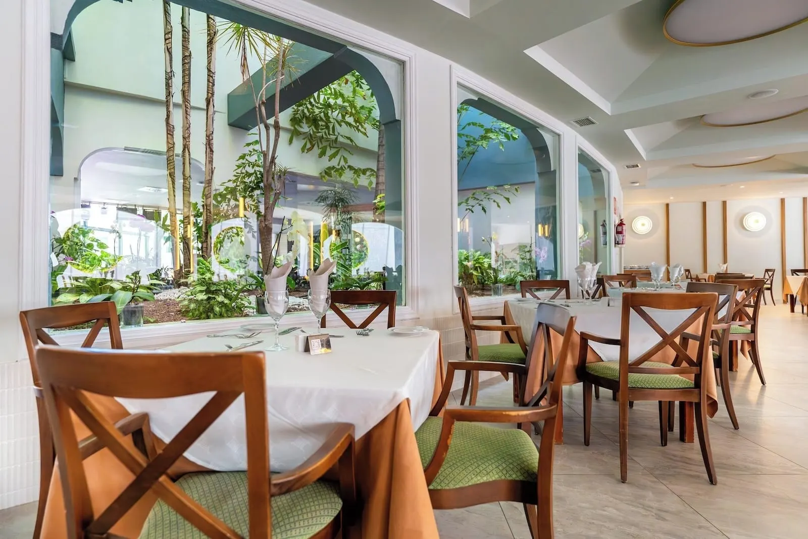 Hotel Colón Guanahaní: A restaurant with wooden chairs and tables, large windows with plants