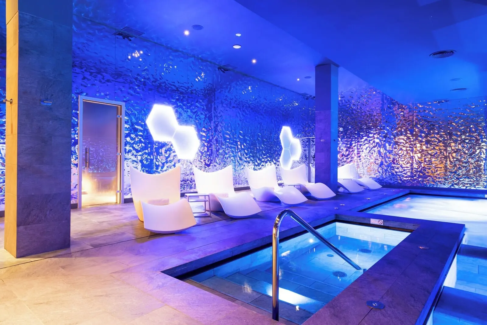 HOVIMA Cool Costa Adeje: A modern indoor pool area with a glass wall, white lounge chairs, and a central pool