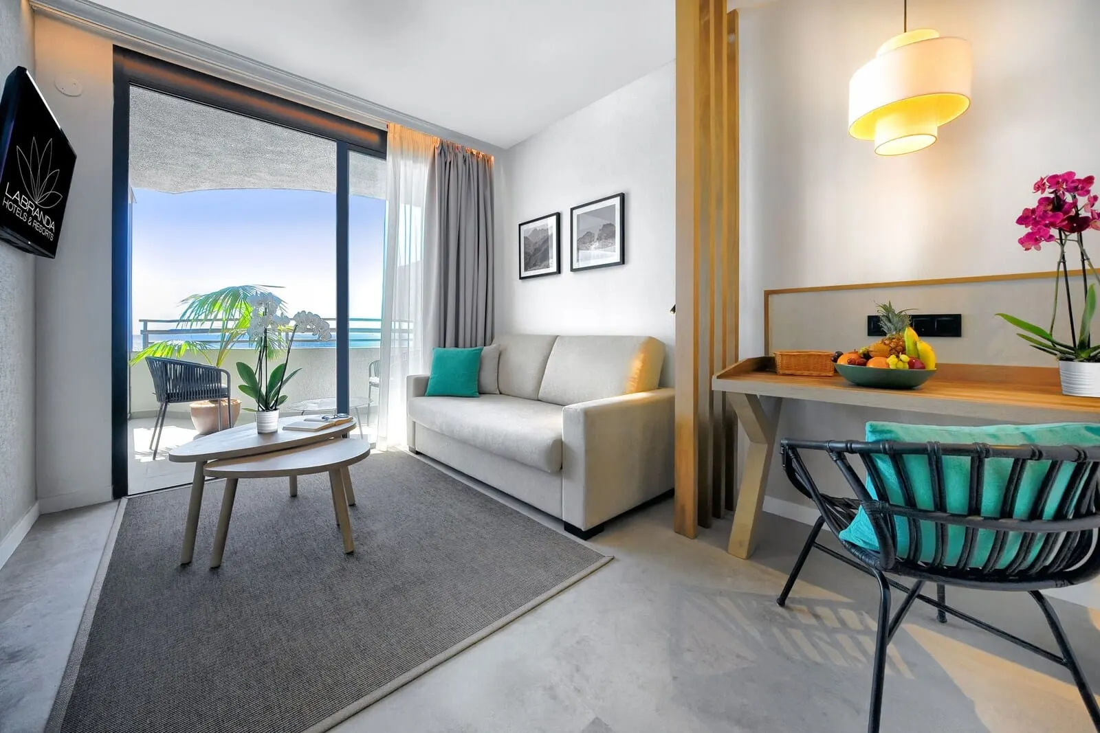 HOVIMA Suites Costa Adeje: A modern hotel room with a balcony, a sofa, a dining table, and a chair