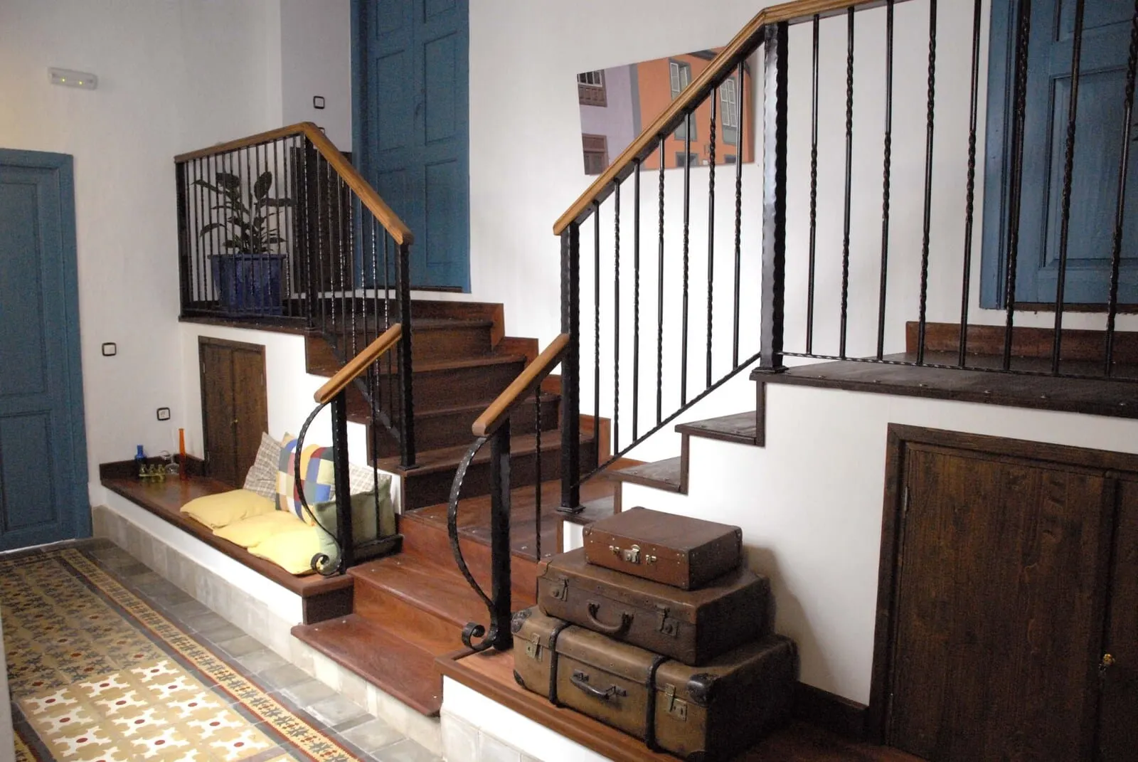 Hotel Cuatro Esquinas: A staircase with wooden steps, black metal railings, and a blue door at the top
