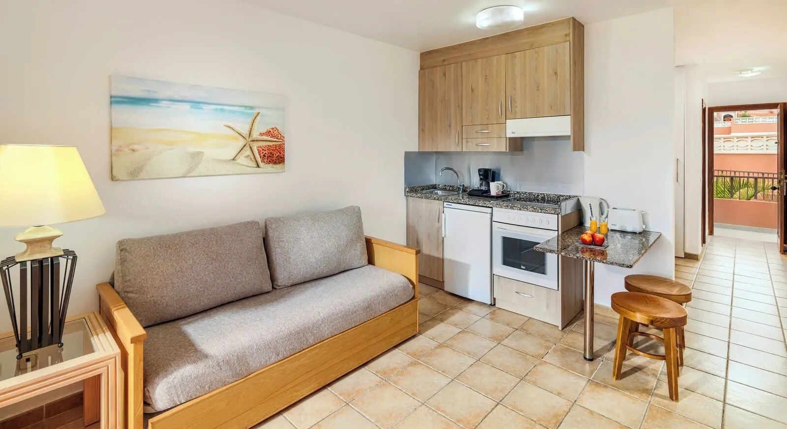 Sol Sun Beach Apartamentos: A compact living space with a sofa, kitchenette, and a painting of a beach scene