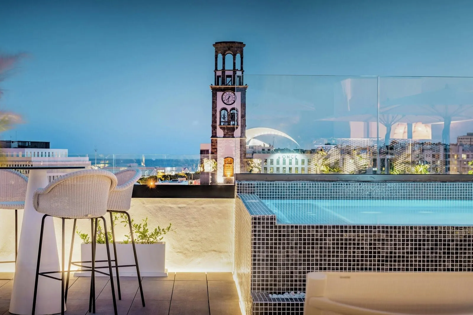 AC Hotel Tenerife: A rooftop bar with a pool, two wicker chairs, and a clock tower in the background