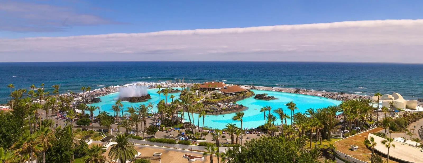 H10 Tenerife Playa: A resort with a central pool, palm trees, and a view of the ocean
