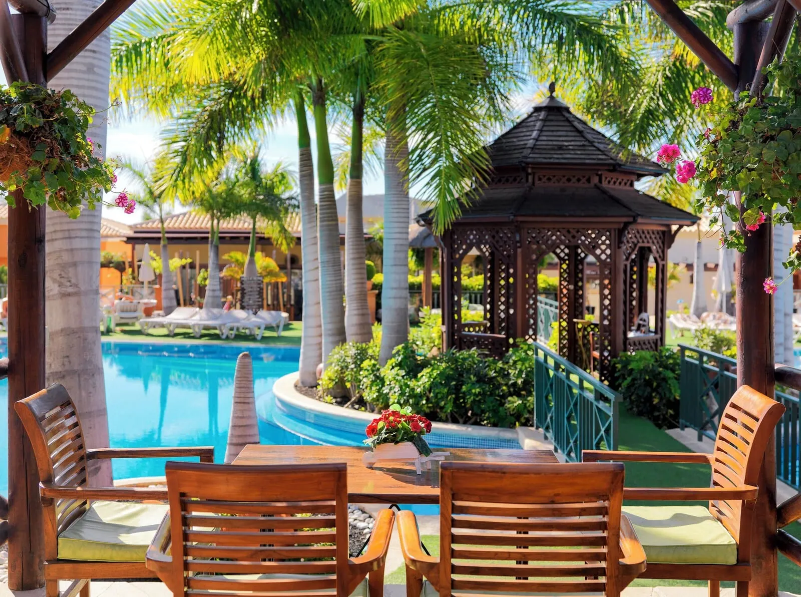 Green Garden Eco Resort & Villas: A poolside area with wooden chairs and a table, surrounded by palm trees and a gazebo