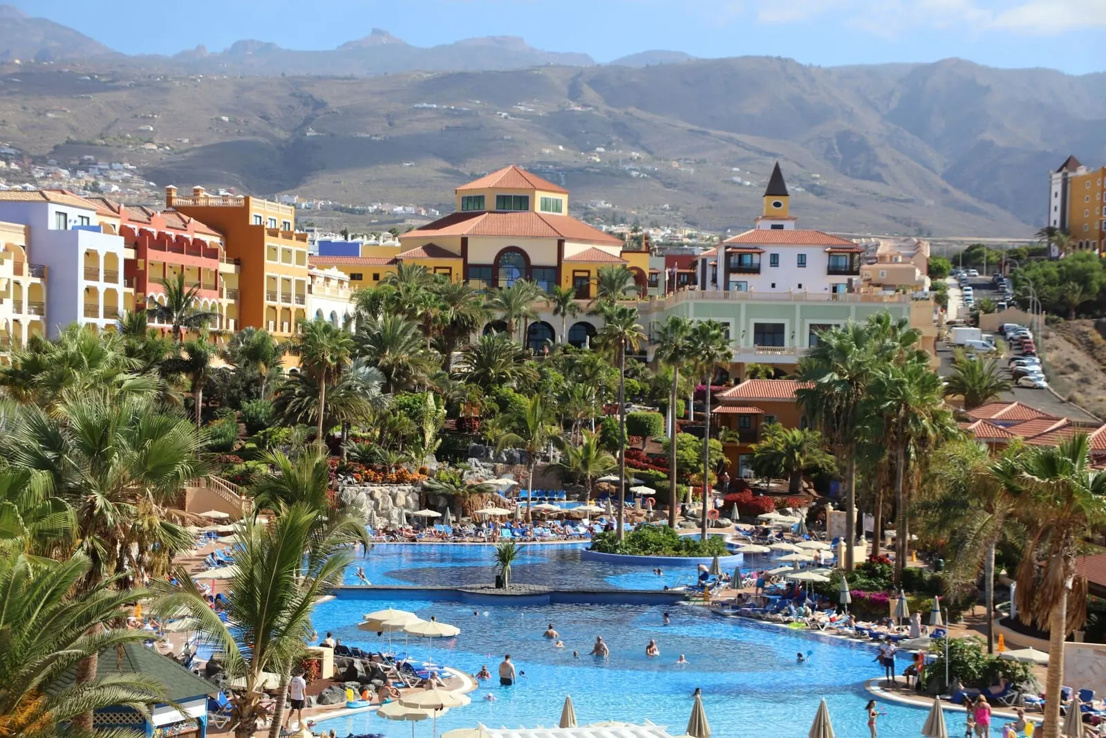 Bahia Principe Explore Costa Adeje: A resort with multiple swimming pools, palm trees, and a mountainous backdrop