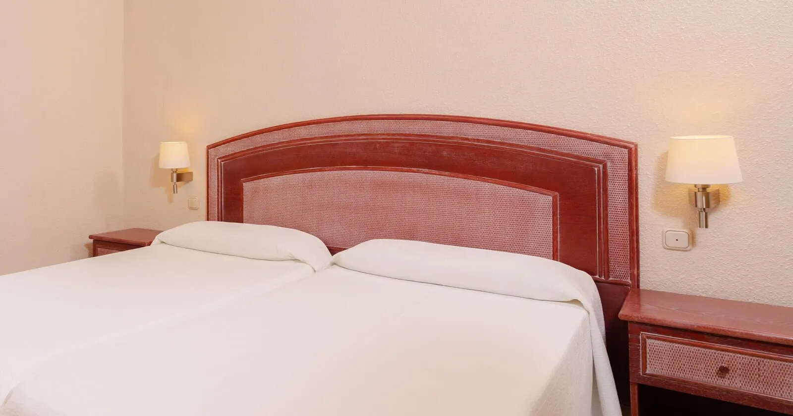 HOVIMA Santa María: A double bed with a wooden headboard, two bedside tables, and wall-mounted lamps