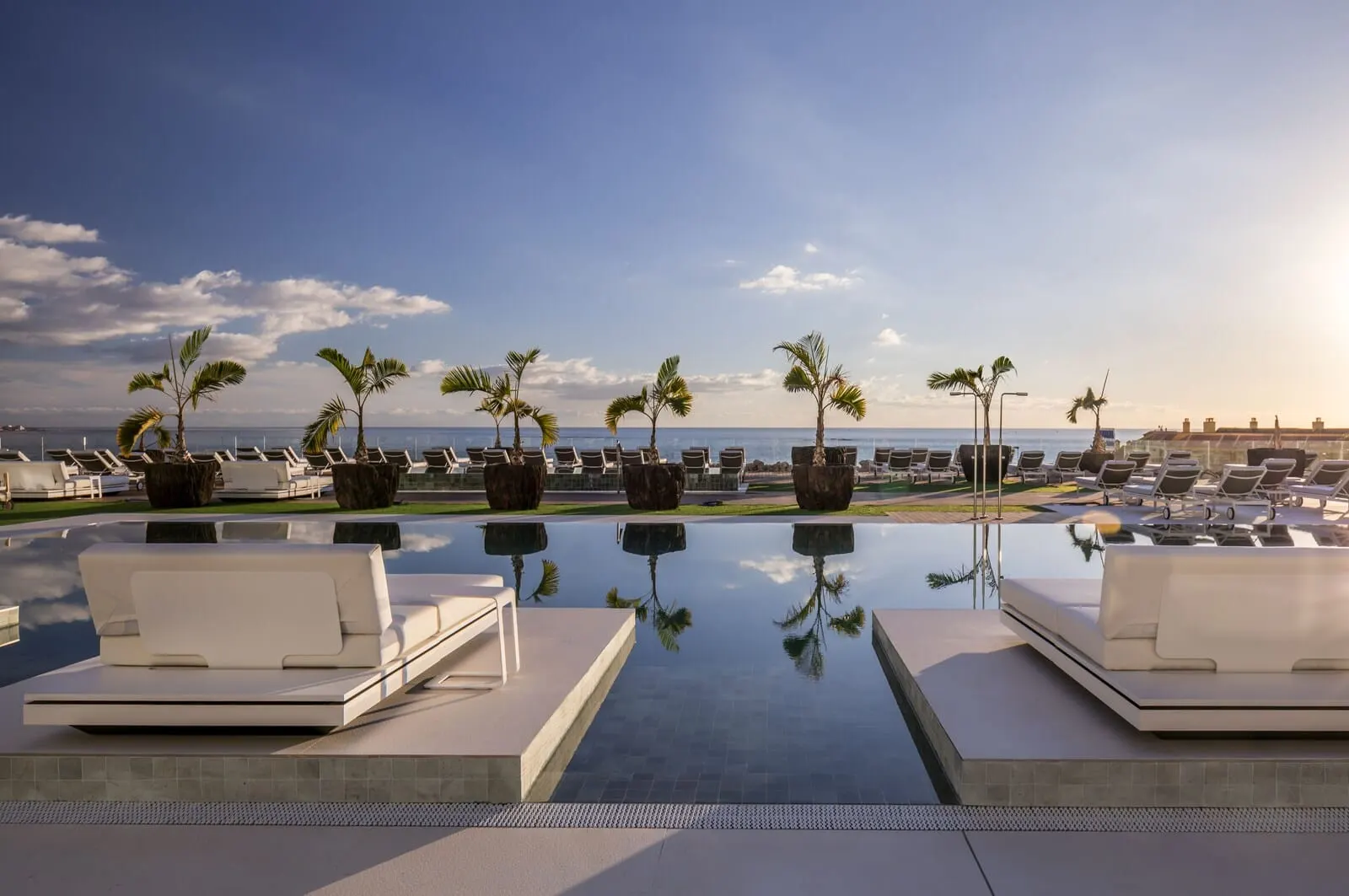 Royal Hideaway Corales Suites: A rooftop infinity pool with lounge chairs and palm trees, offering a view of the ocean