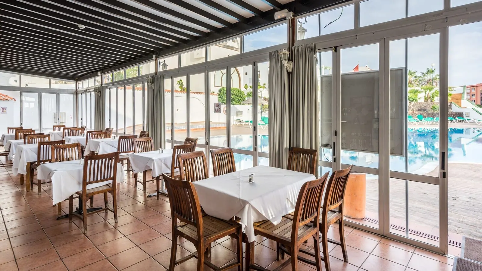 BLUESEA Callao Garden: A restaurant with tables and chairs, large windows, and a view of a swimming pool