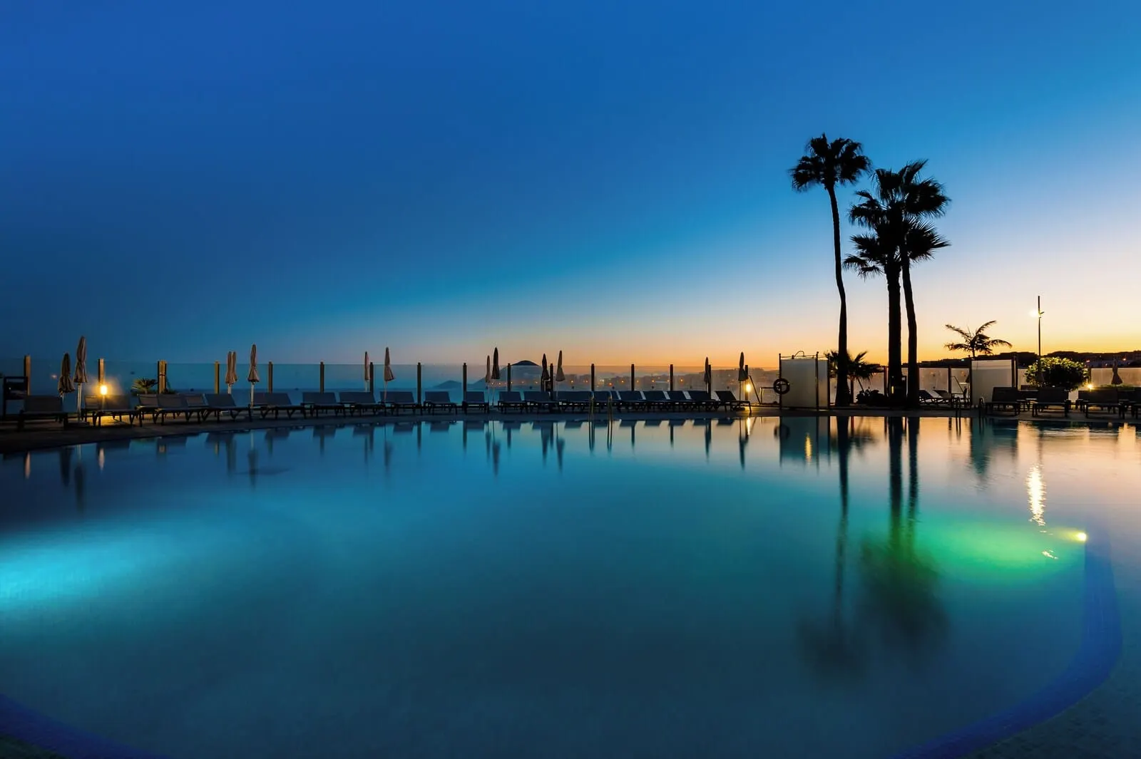 KN Hotel Arenas del Mar: A calm pool area with lounge chairs and palm trees, reflecting the sunset
