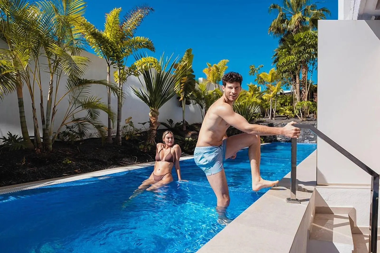 MYND Adeje: A man and a woman in a swimming pool with palm trees and a clear sky in the background