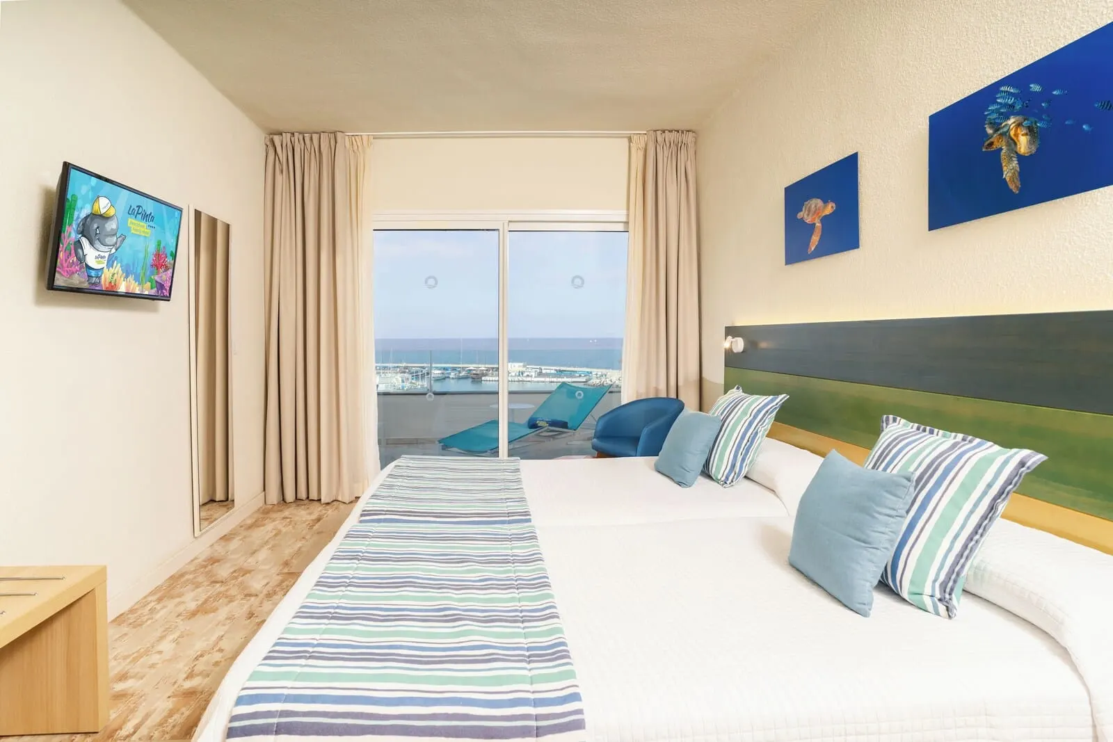 HOVIMA La Pinta Beachfront Family Hotel: A hotel room with a large bed, a view of the sea, a TV, and artwork on the walls