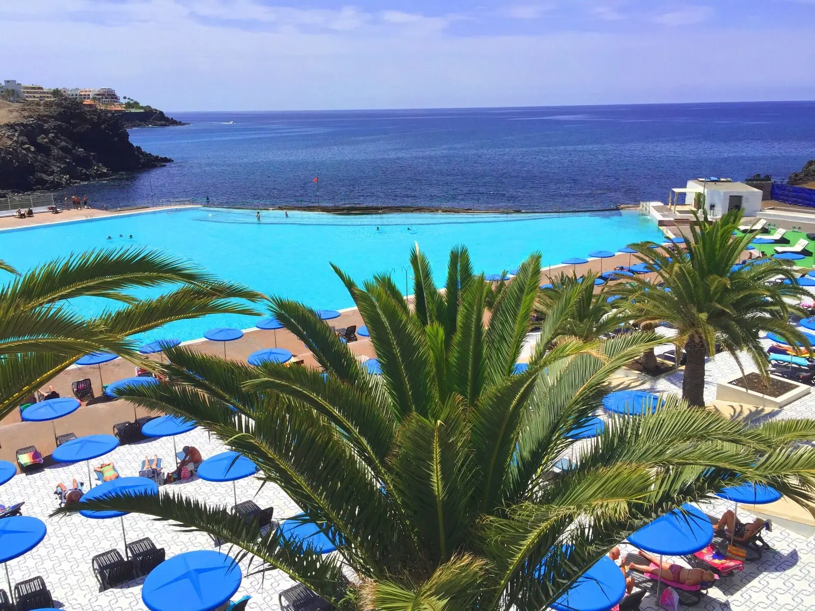 Ona Alborada: A pool area with blue umbrellas and lounge chairs, overlooking a clear blue sea