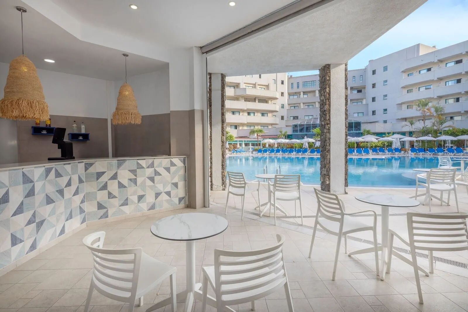 Alua Tenerife: A poolside area with white chairs and tables, a tiled wall with geometric patterns