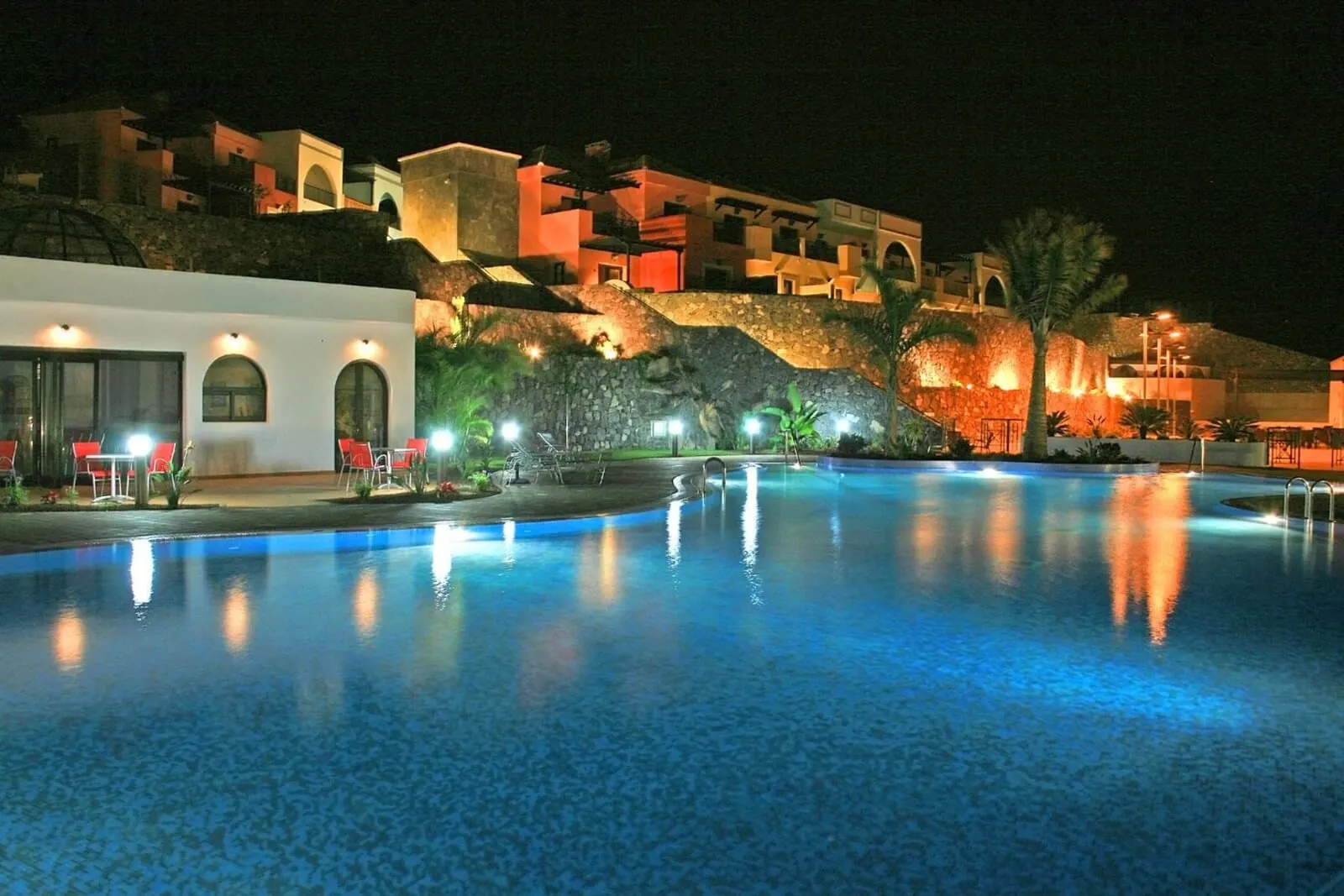 Hotel Luz del Mar: A nighttime view of a swimming pool with a stone wall and red chairs
