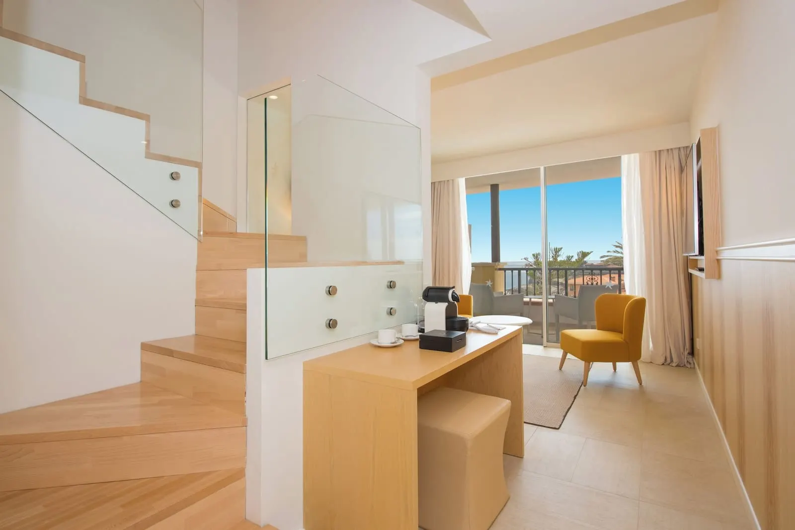 Iberostar Selection Anthelia: A modern hotel room with a wooden staircase, a glass-enclosed desk, a yellow armchair