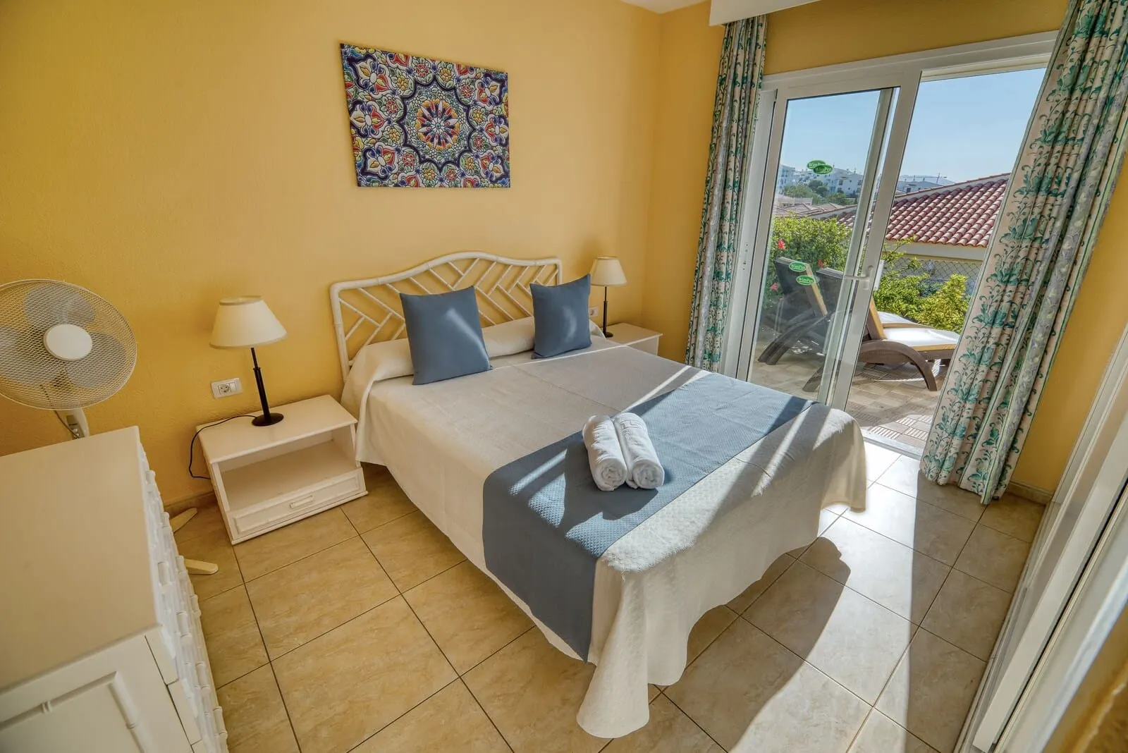 Ona Sueño Azul: A hotel room with a bed, two bedside tables, a fan, a window with curtains