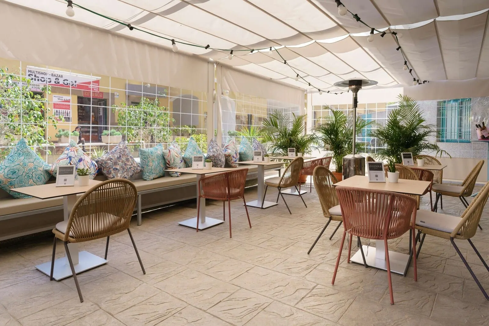 Alua Tenerife: An indoor seating area with tables and chairs, large windows, and potted plants