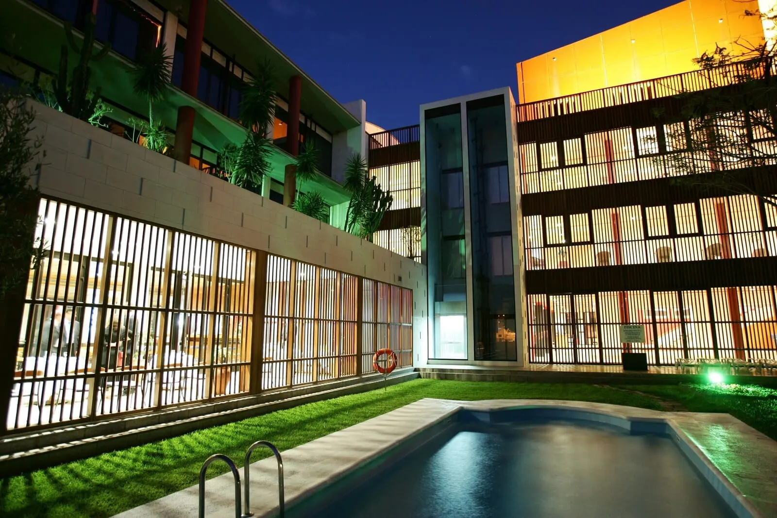 Hotel Escuela Santa Cruz: A modern hotel with a swimming pool, outdoor seating, and a well-lit facade
