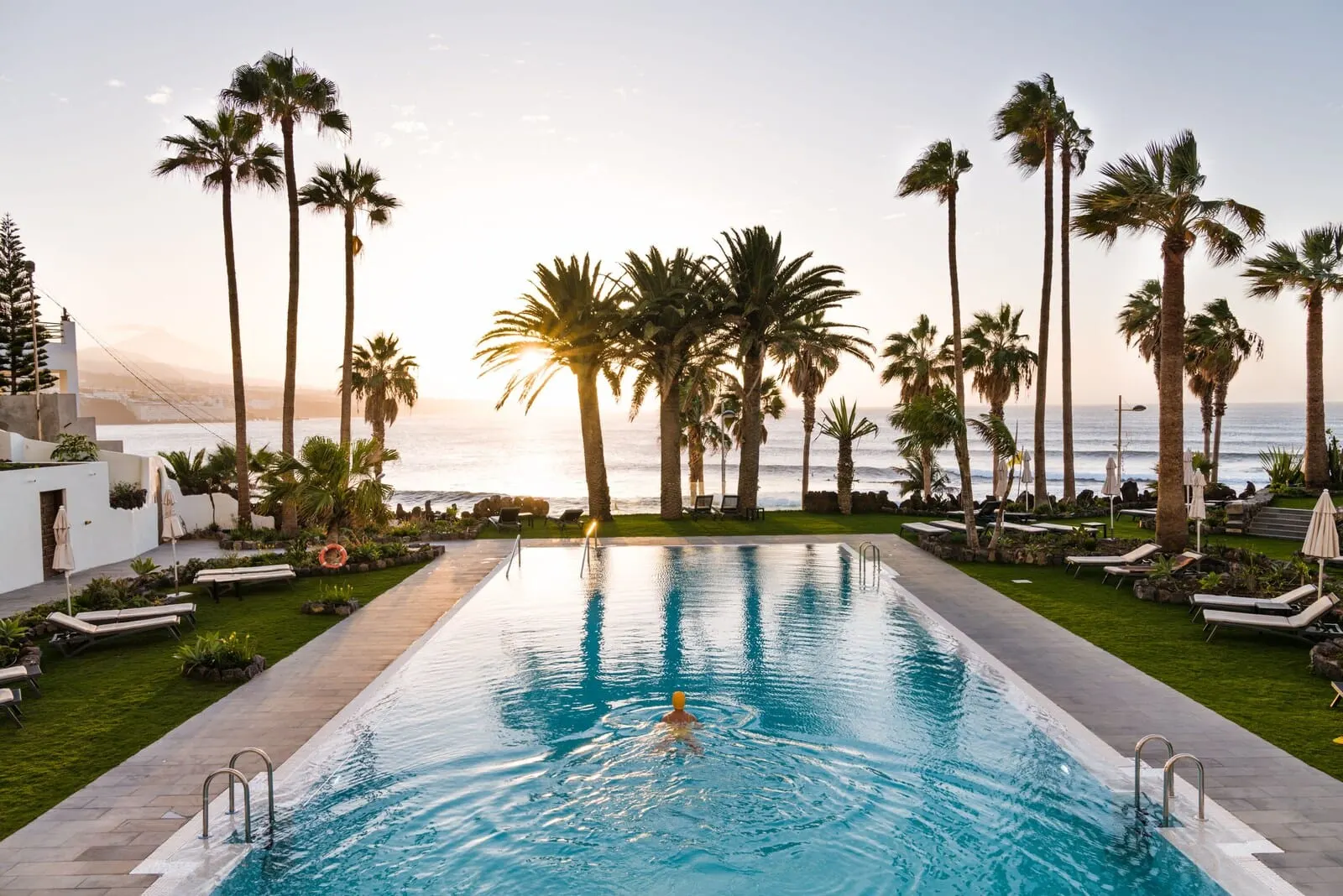 Océano Health Spa Hotel: A swimming pool with a person swimming, surrounded by palm trees and lounge chairs