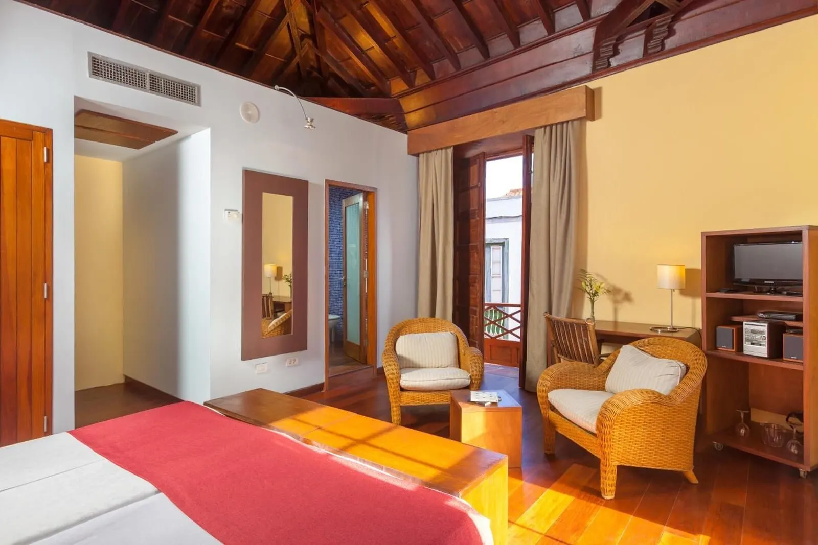 Hotel La Quinta Roja: A hotel room with a wooden ceiling, a bed with a red blanket, two wicker chairs