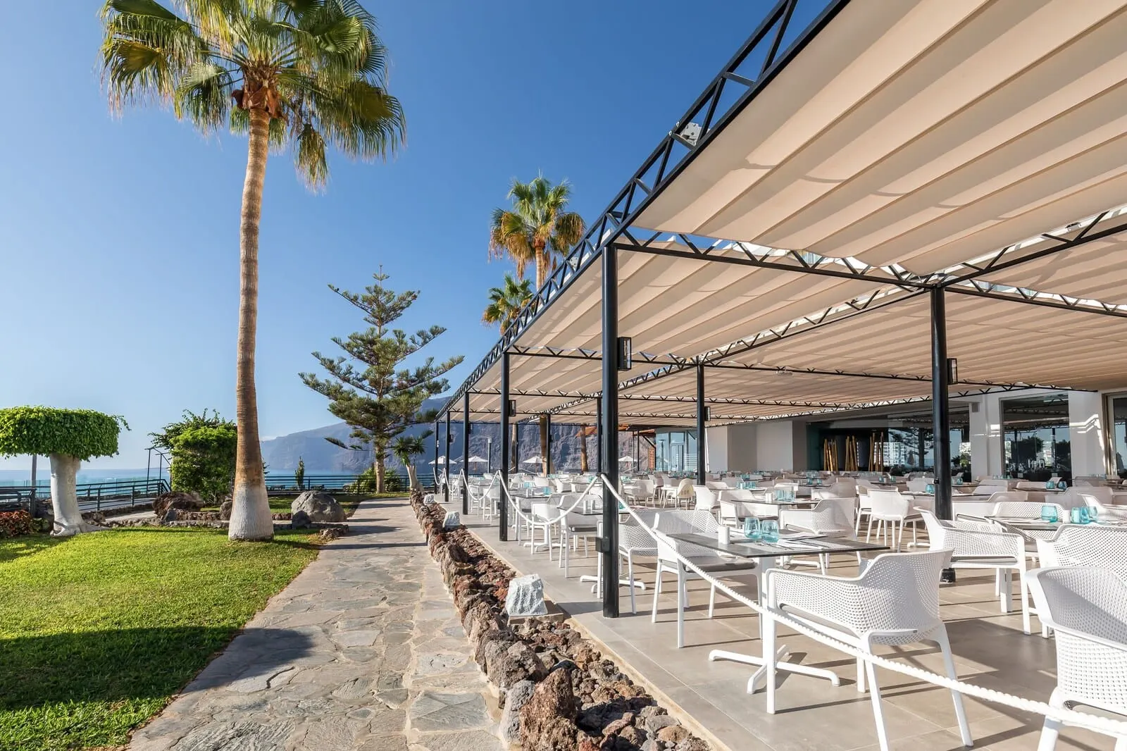 Barceló Santiago: An outdoor seating area with white chairs and tables, a stone pathway, and palm trees